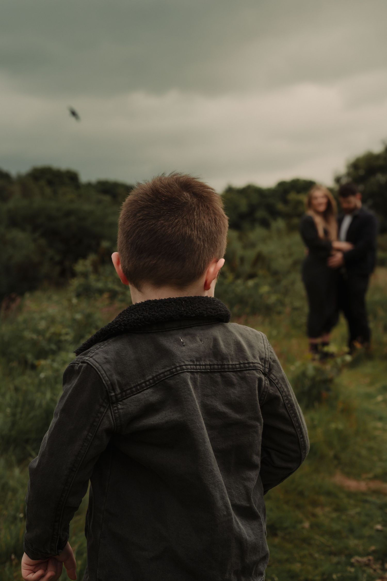 A person wearing a dark denim jacket stands in a green field on an overcast day.