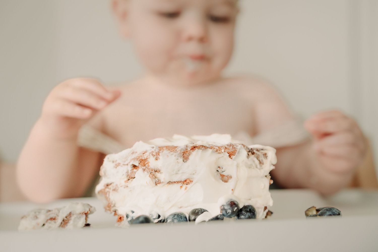 A series of photos showing a baby's hands reaching for and smashing into a white frosted birthday cake.