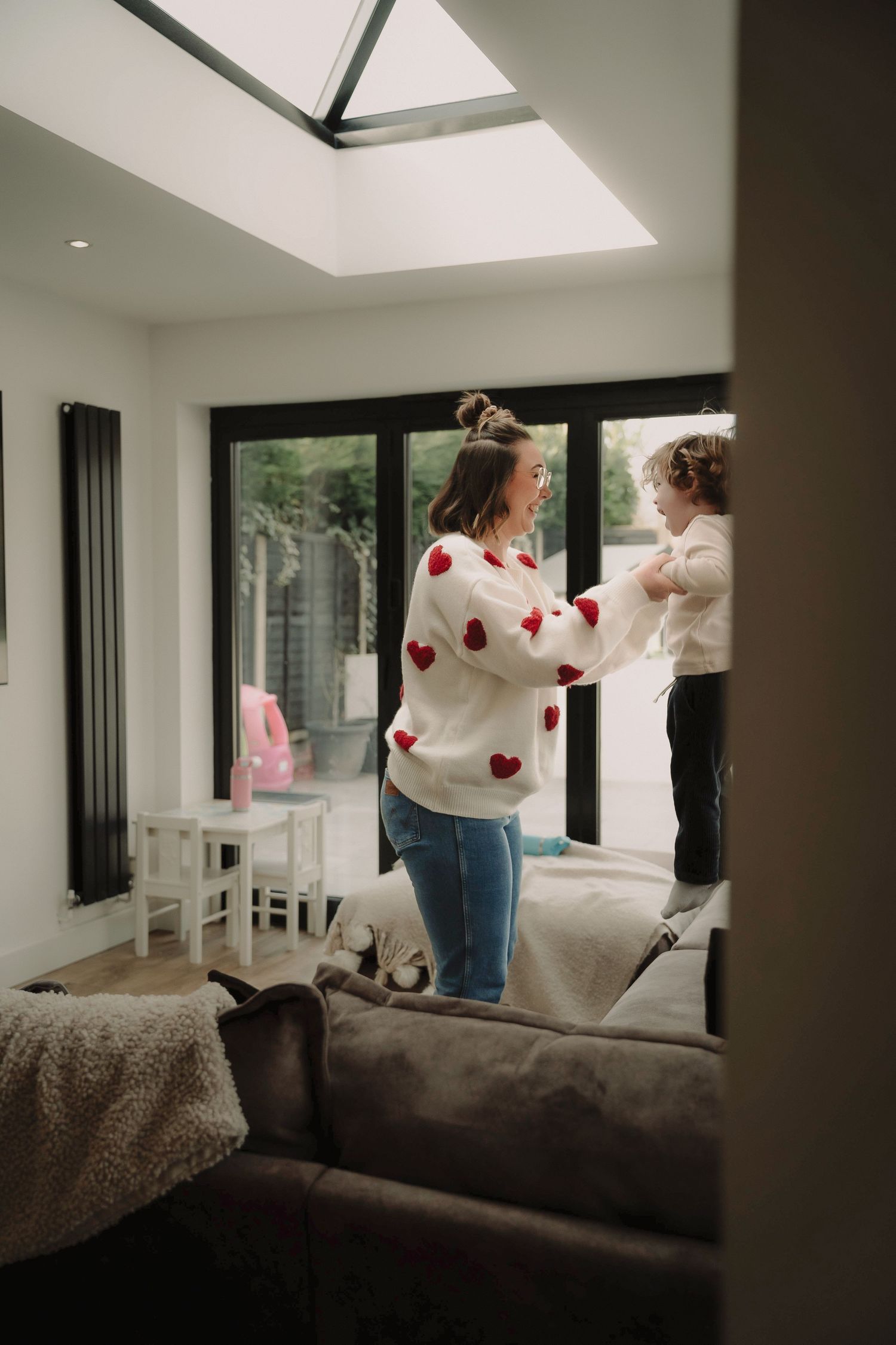 A sequence of photos showing someone in a white sweater with red hearts dancing and jumping on a couch in a modern room.