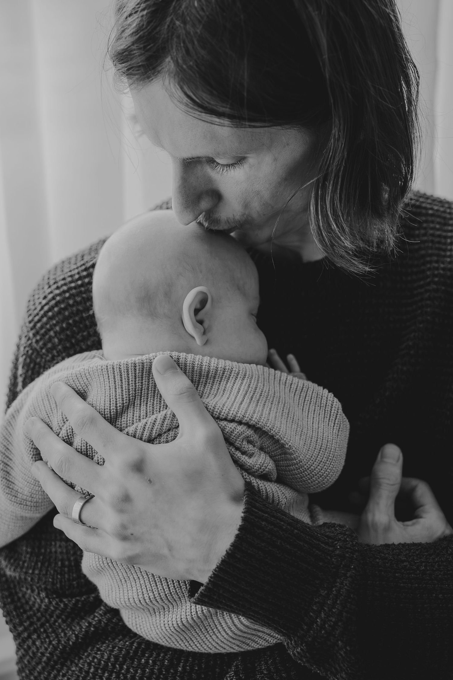 An intimate black and white portrait of a tender moment with a baby in a knit sweater.