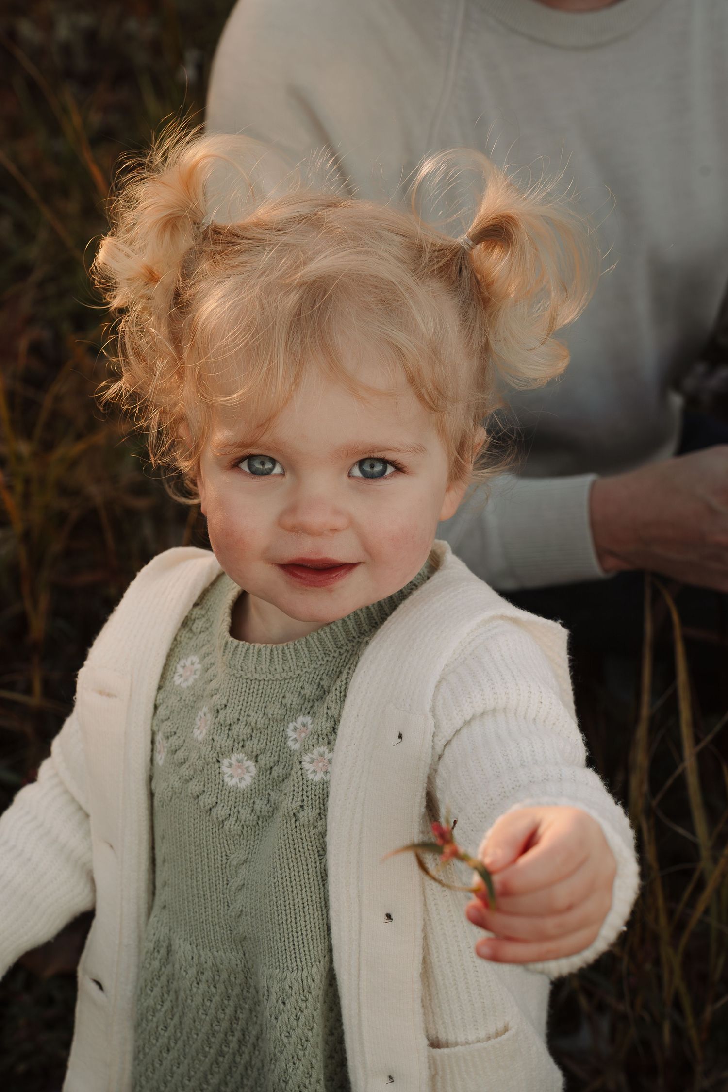 Close-up shots of a toddler wearing a sage green sweater and white cardigan.