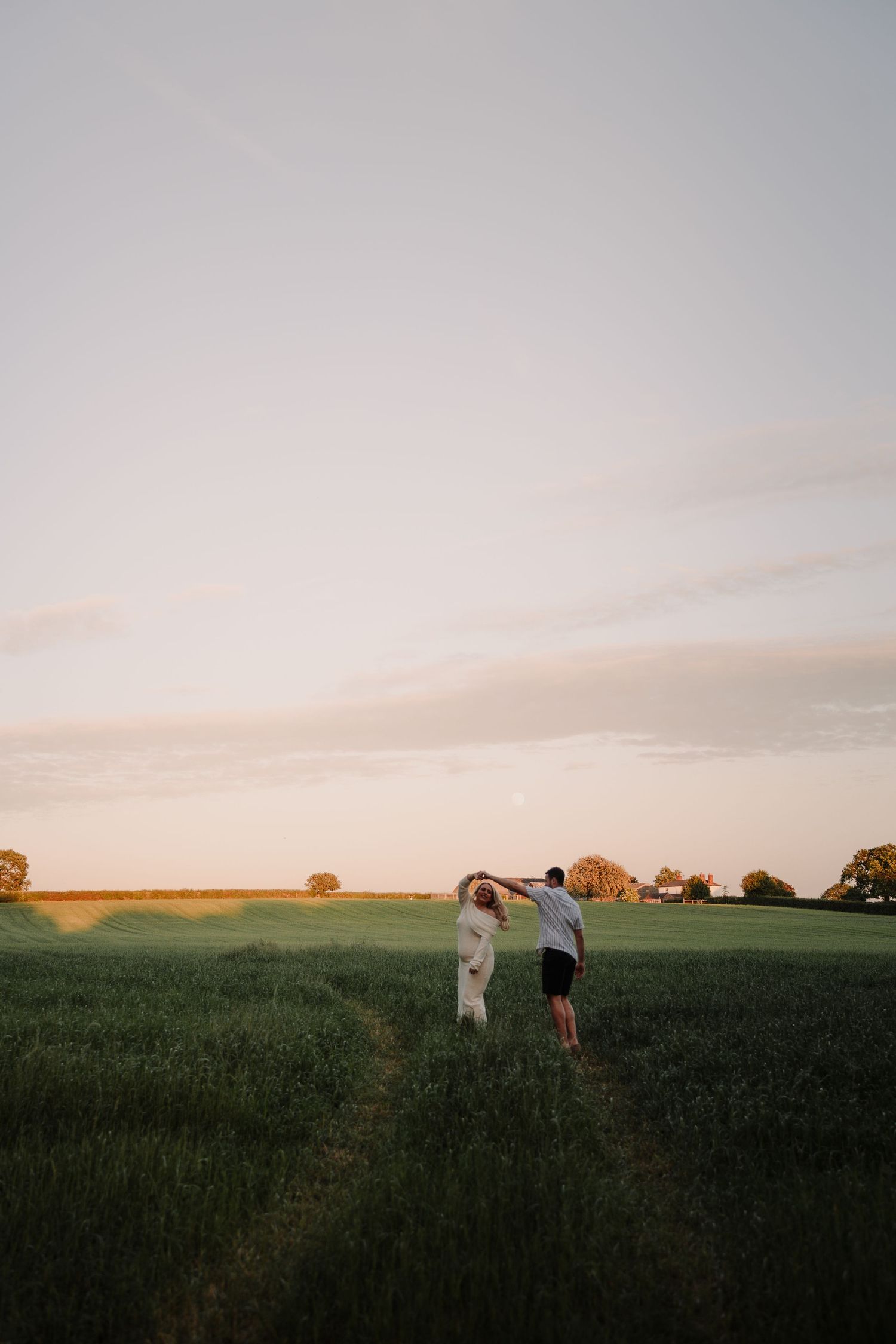 Couple walking hand in hand through a lush green field at golden hour sunset.
