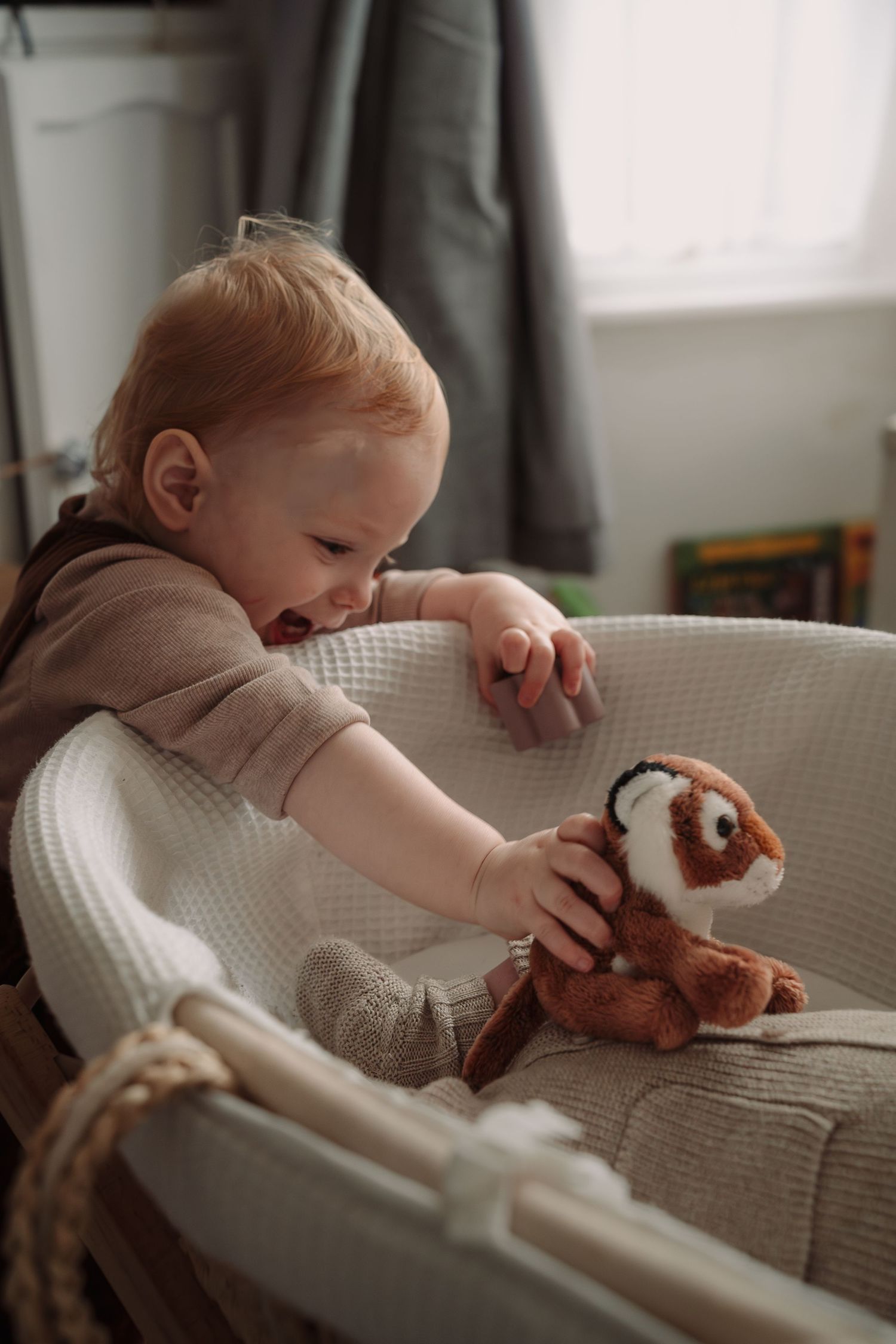 Small child reaches for stuffed toy while playing on white couch.