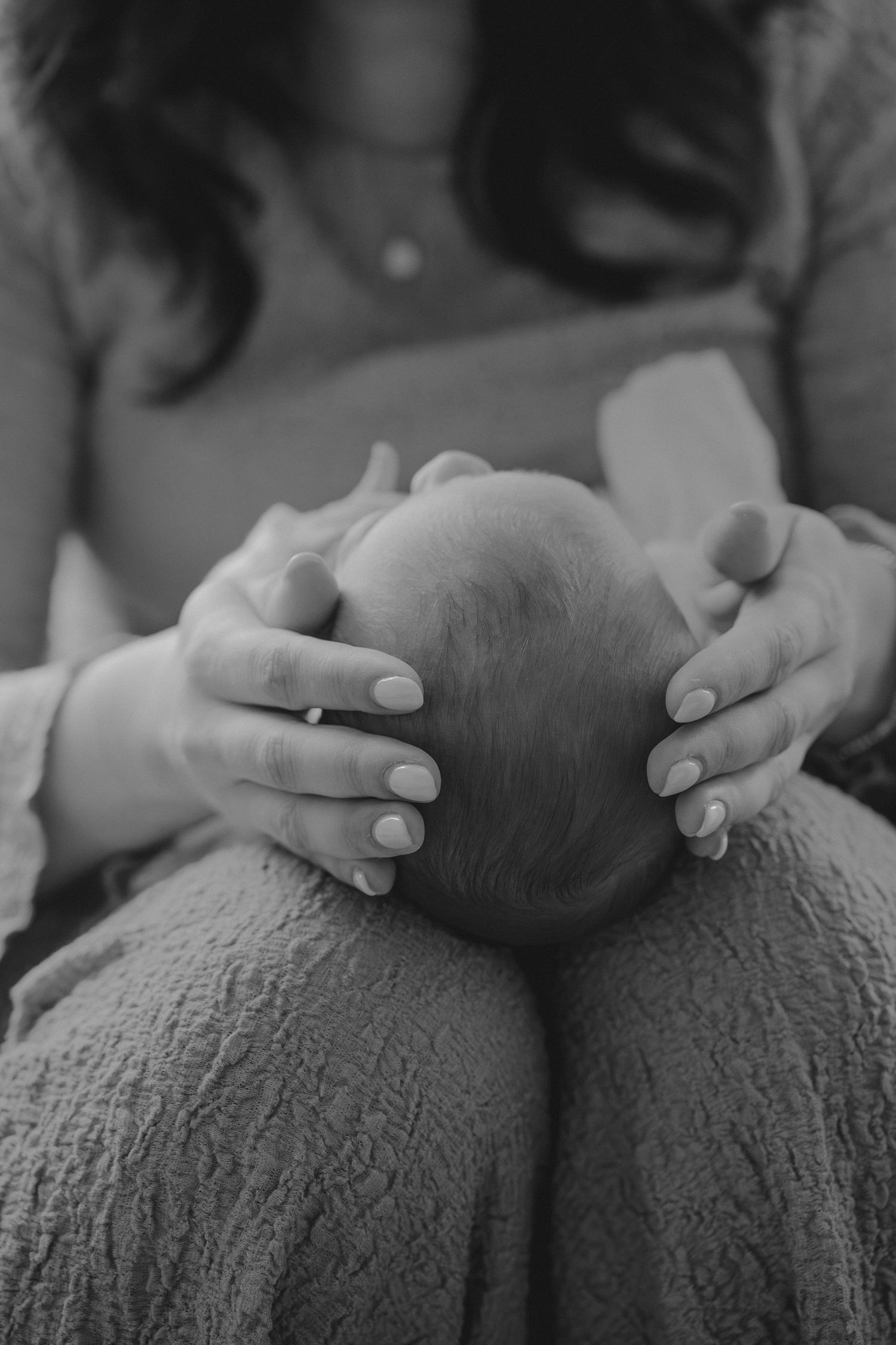 Black and white photo of mother cradling newborn babys head.