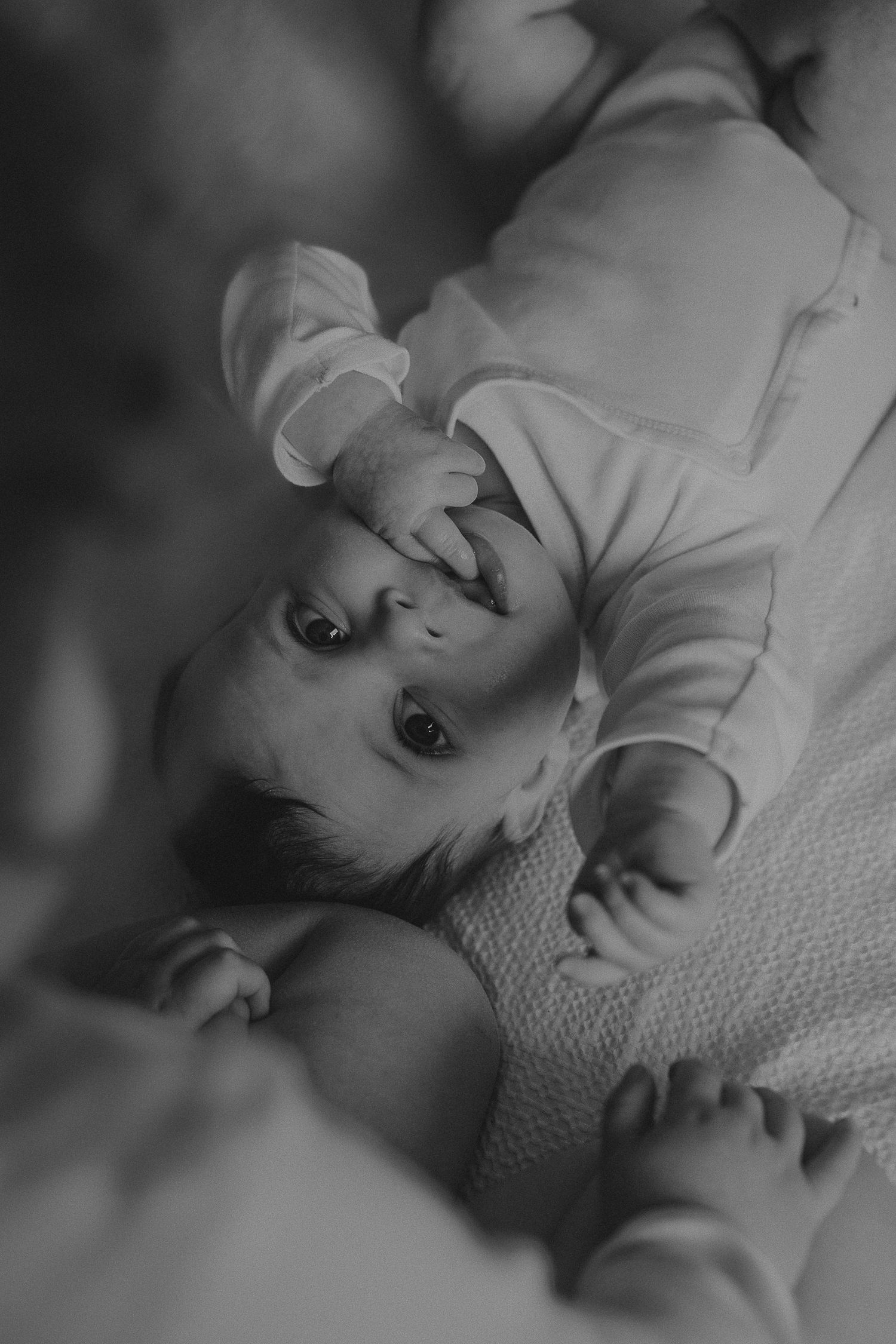 Black and white portrait of a baby lying on textured fabric.