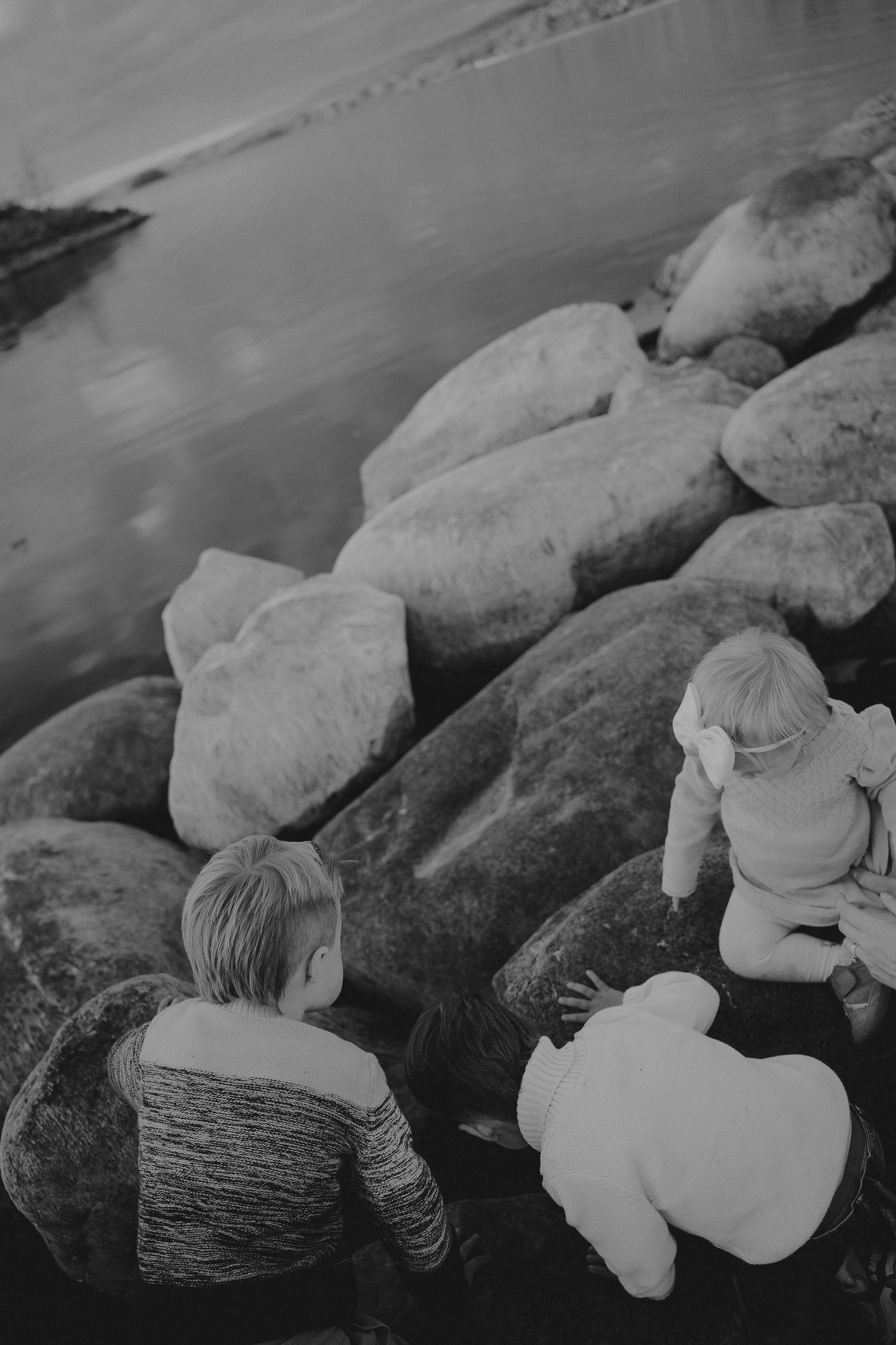 Black and white series showing small children looking over large rocks by the water During a Tamworth family session.