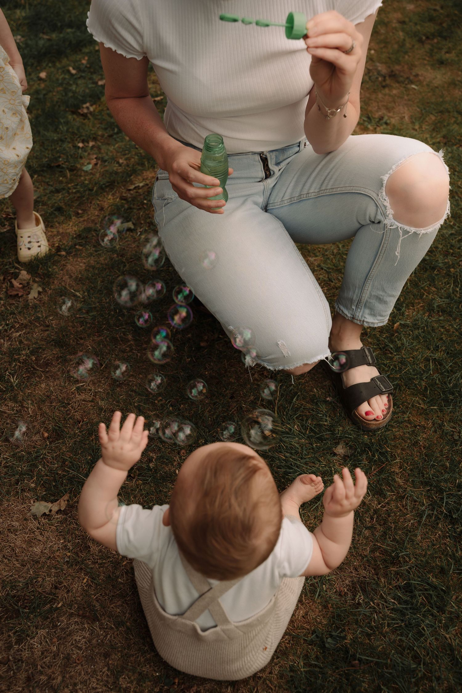 A small child in a white shirt sits on grass while playing with a green toy.