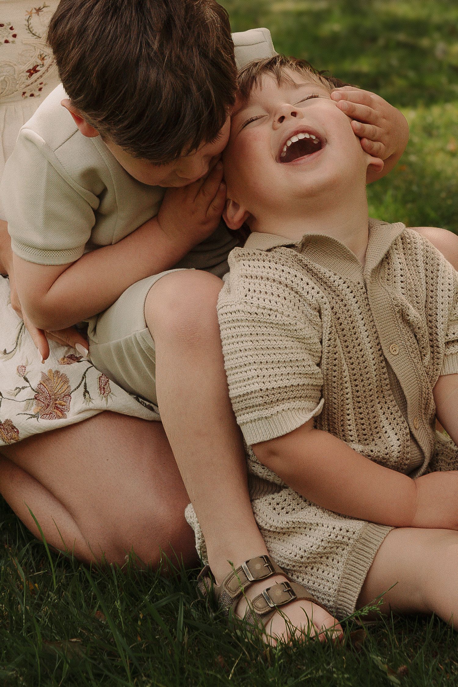 Tamworth family photography showing two children lying on grass sharing playful moments of laughter and affection in matching outfits.