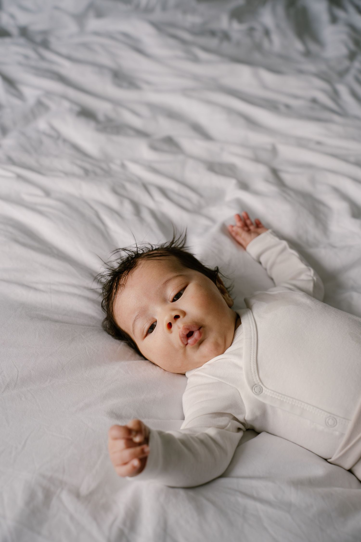 Peaceful baby sleeping soundly on white bedding in natural light.