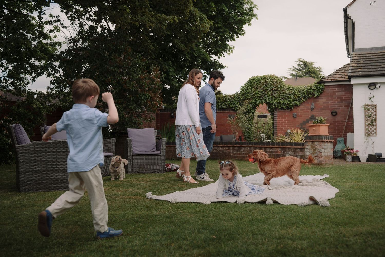 Family enjoying a sunny day in backyard garden with children playing and a golden retriever on a white blanket.