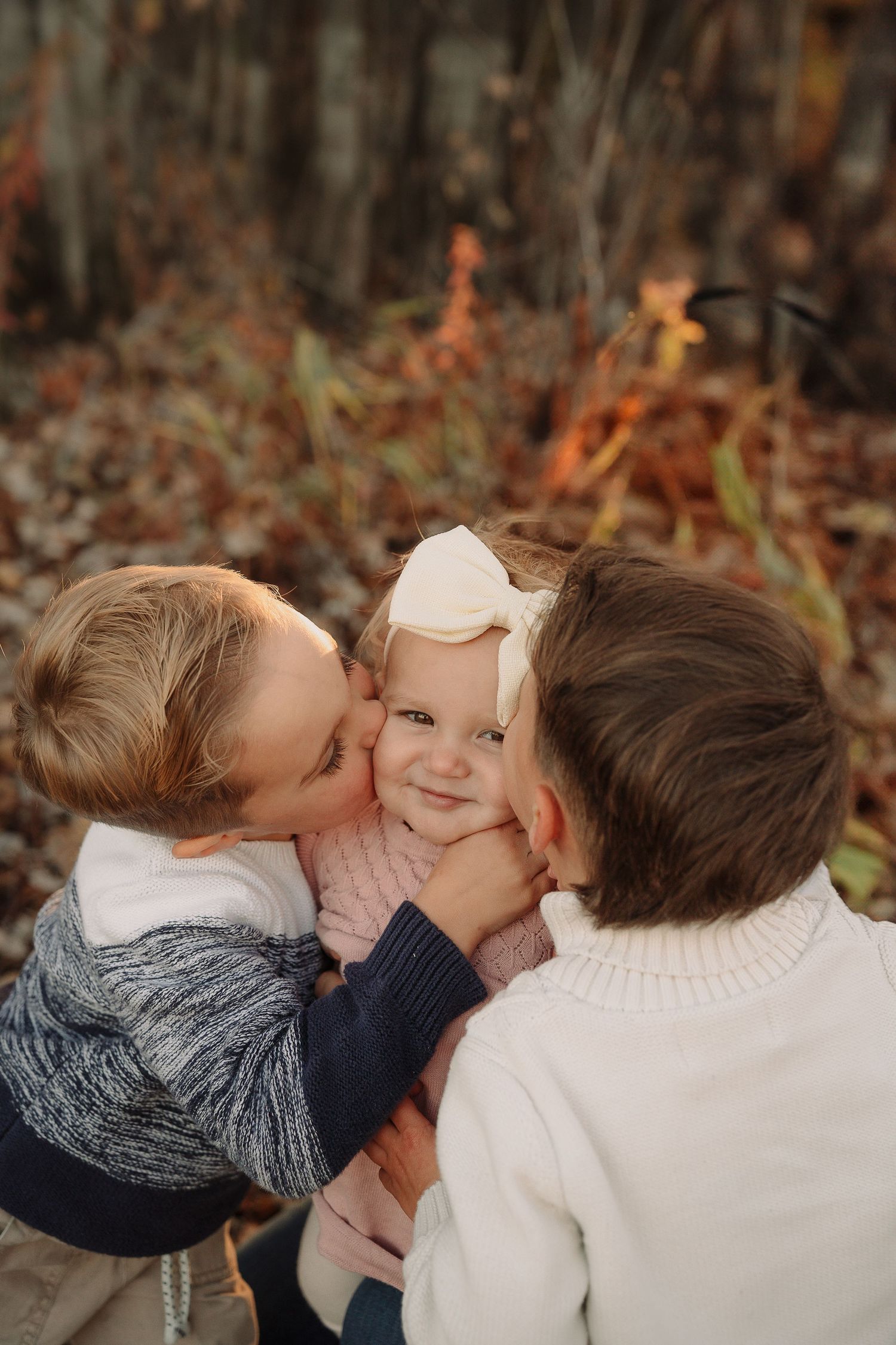 Siblings sharing sweet kisses outdoors in fall setting.