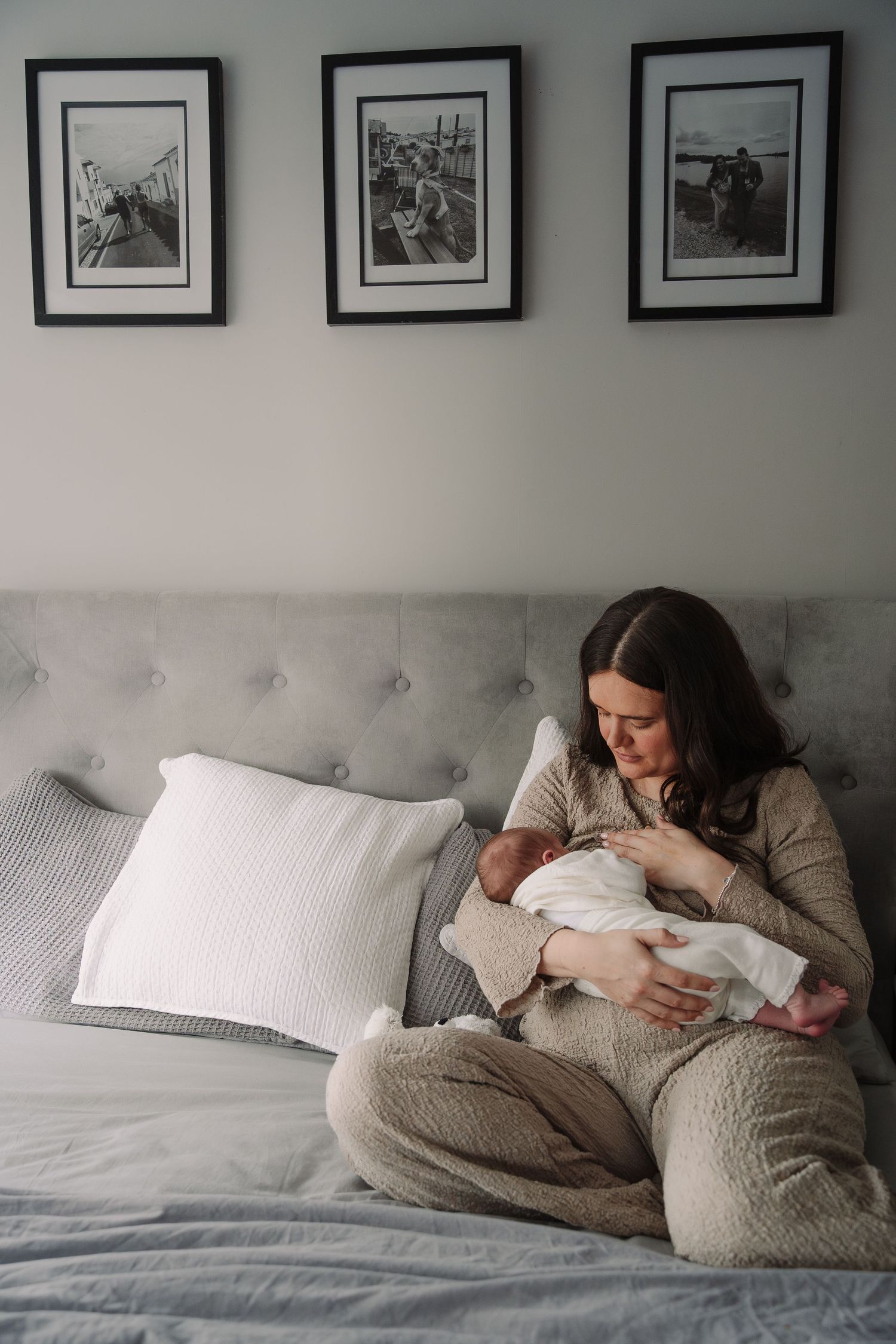 Mother sitting on bed cradling newborn baby in cozy bedroom.
