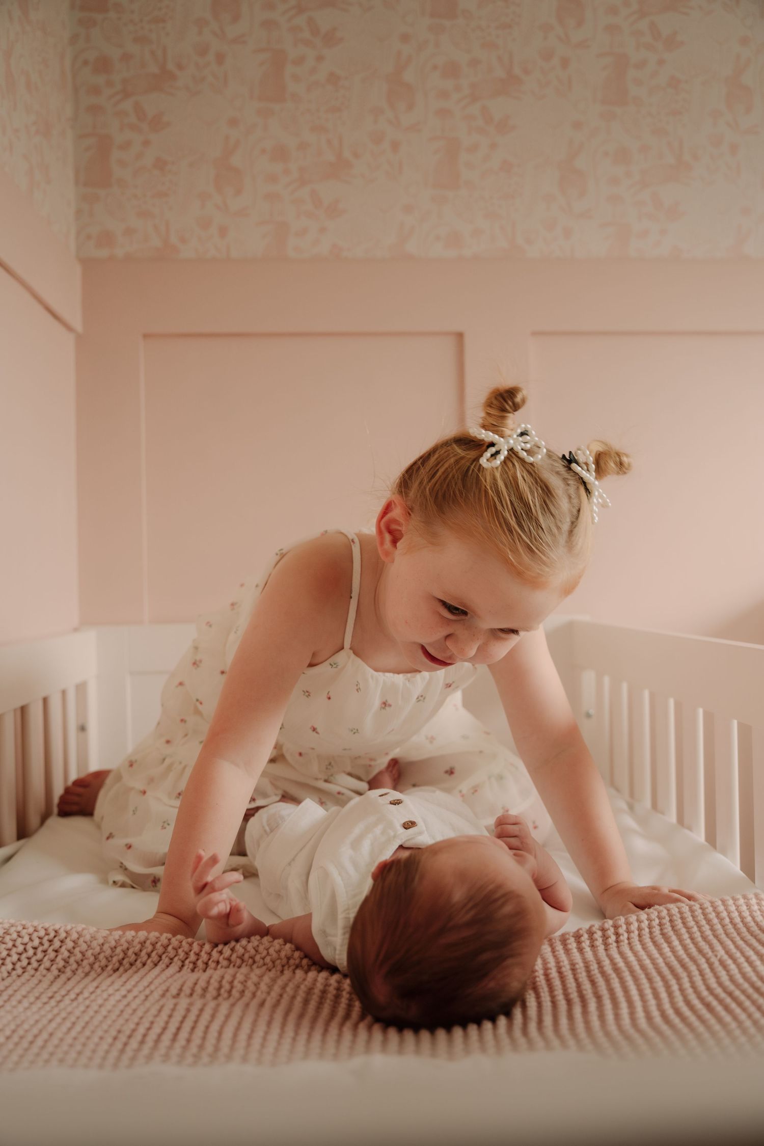 Sweet interaction between siblings on a white bed with soft lighting.