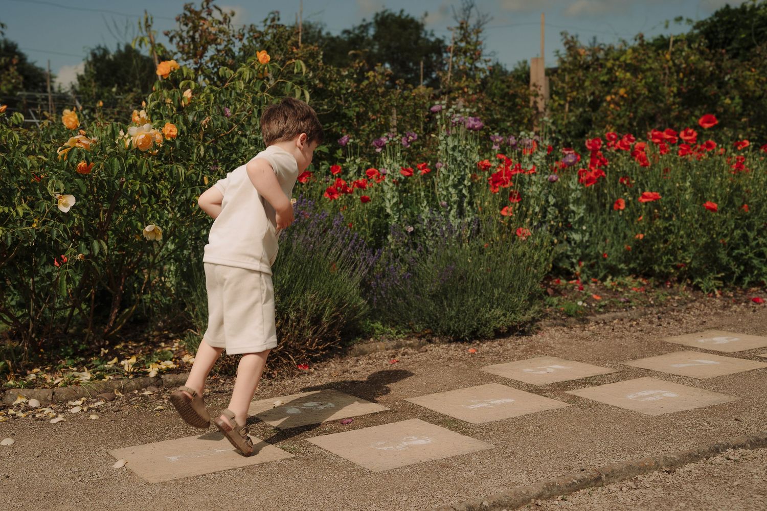 Child in light clothing doing hopscotch with blooming red poppies and greenery in the background by a Tamworth family photographer.
