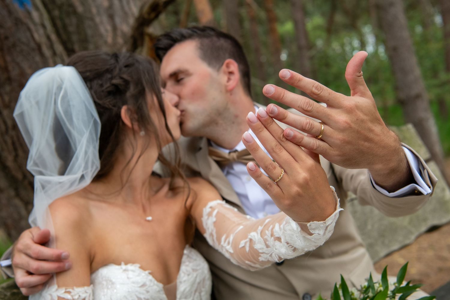 A couple in wedding attire share an intimate moment as they embrace in a wooded setting.