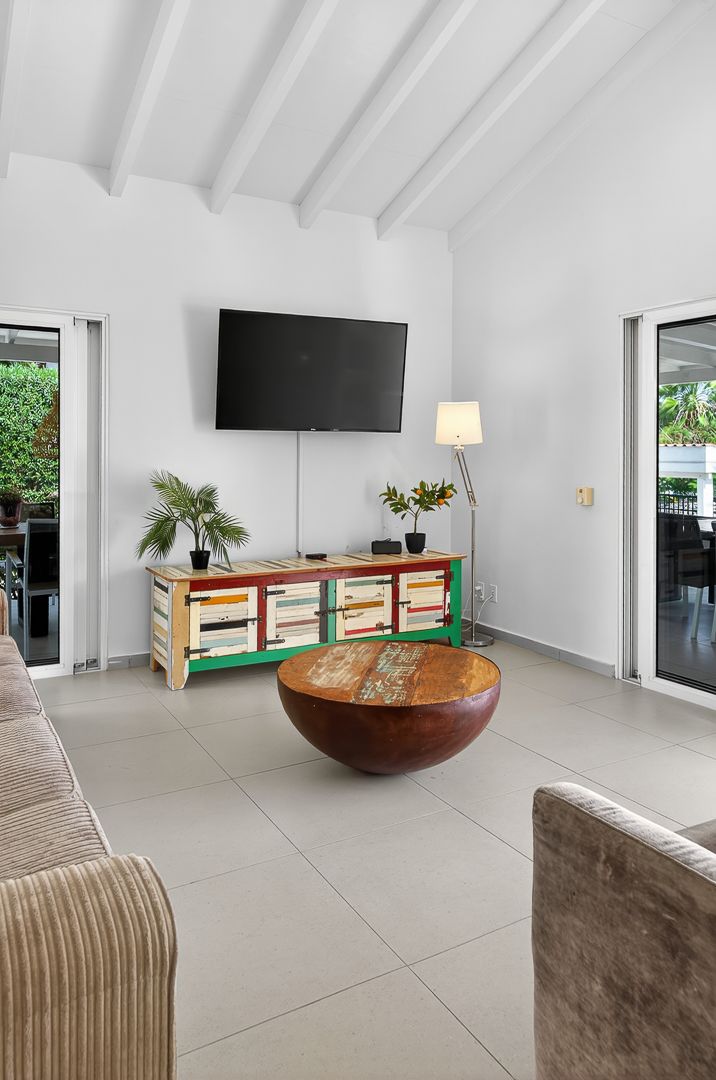 Modern living room with colorful TV console, round wooden coffee table, wall-mounted TV, and vaulted white ceiling.
