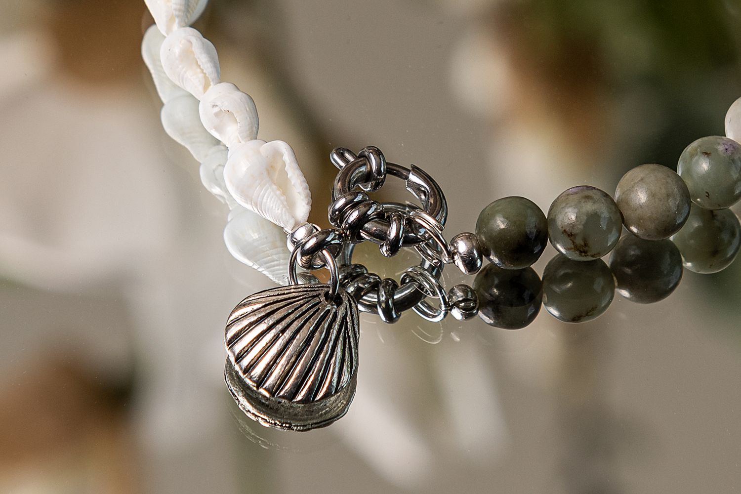 Close-up of a silver shell charm pendant on a beaded necklace with white and gray pearls.
