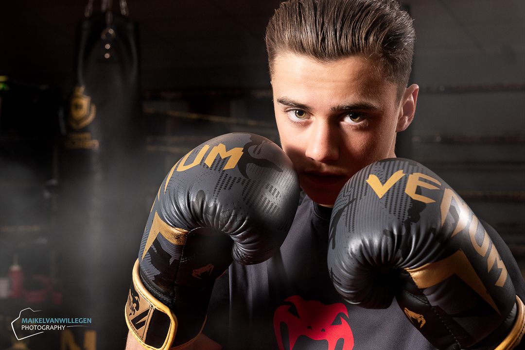Boxer wearing black and gold boxing gloves poses in dramatic studio lighting with dark background.