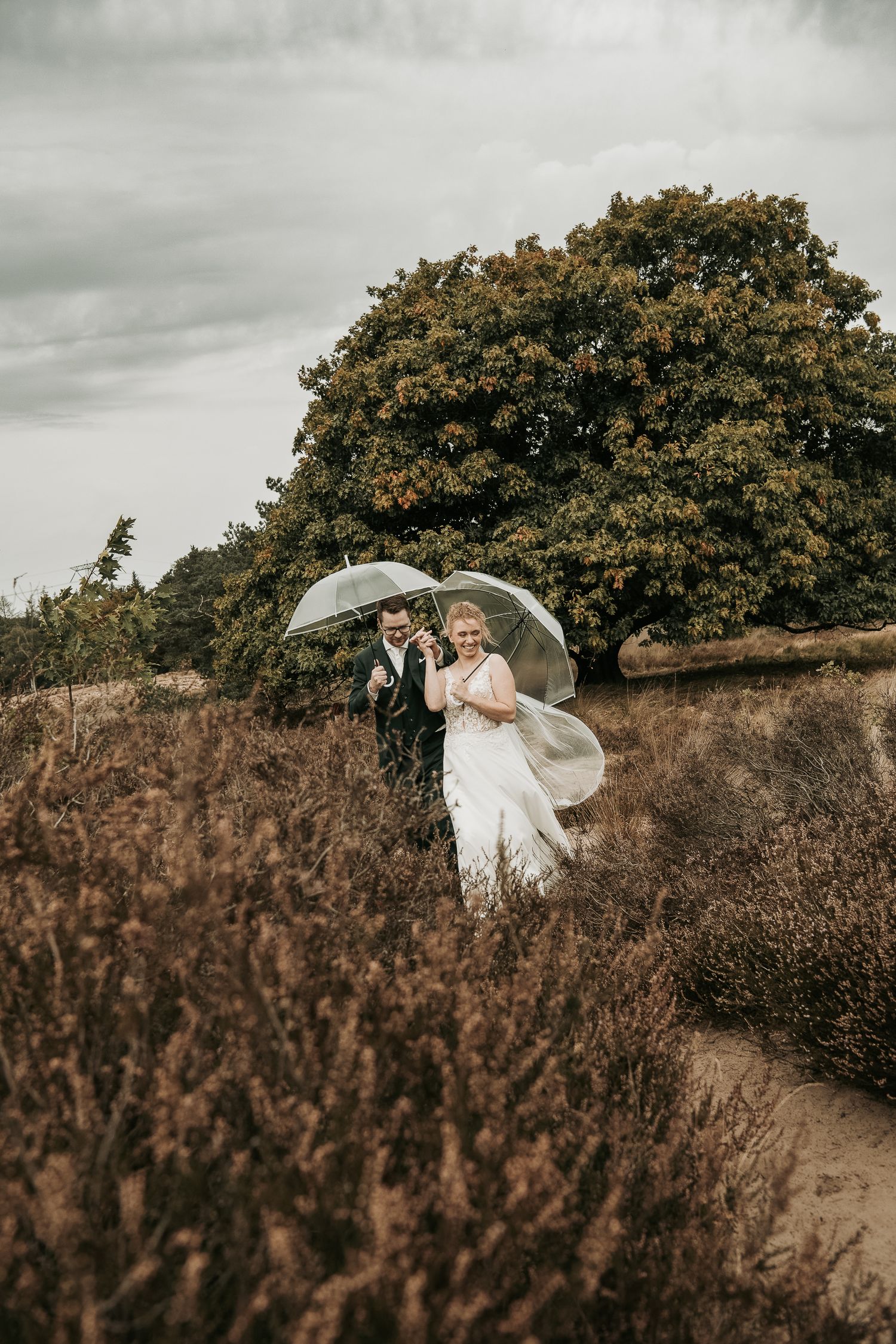 A couple shares an intimate moment under a white umbrella against a moody sky and autumn foliage background.