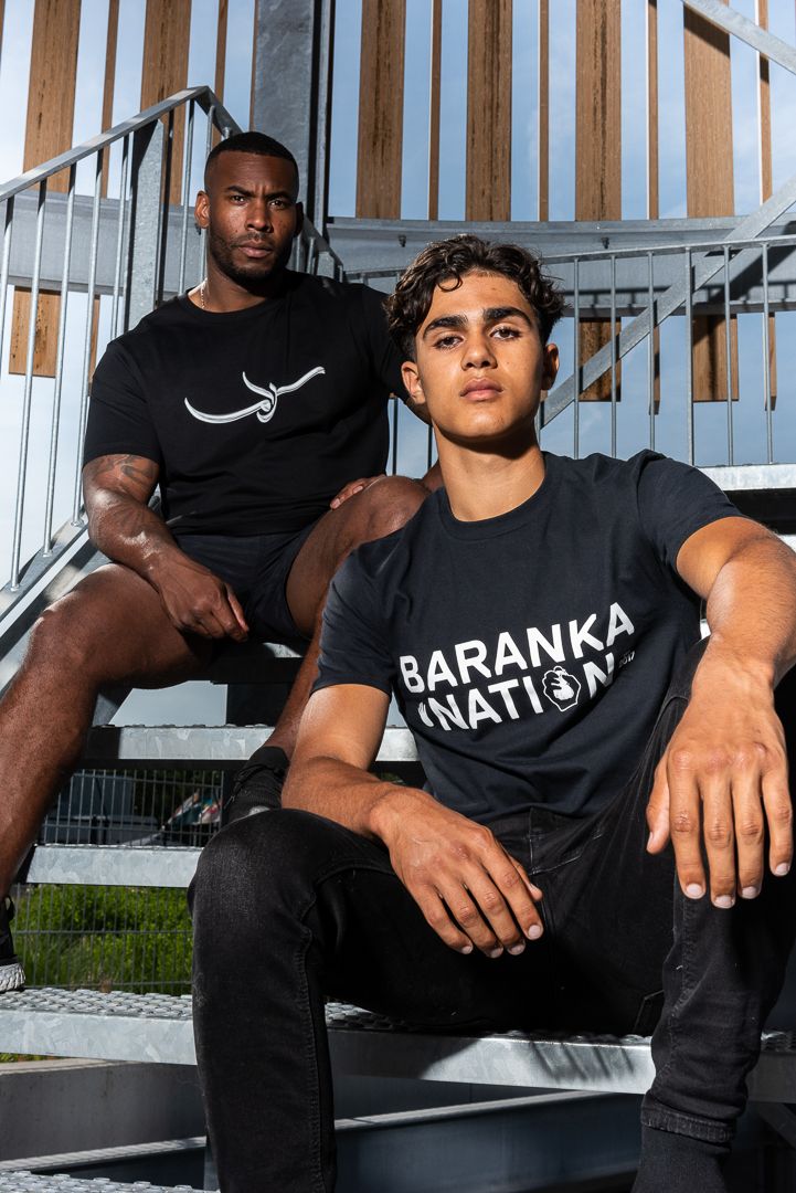 Two models wearing black t-shirts from an athletic apparel brand pose on outdoor metal stairs.