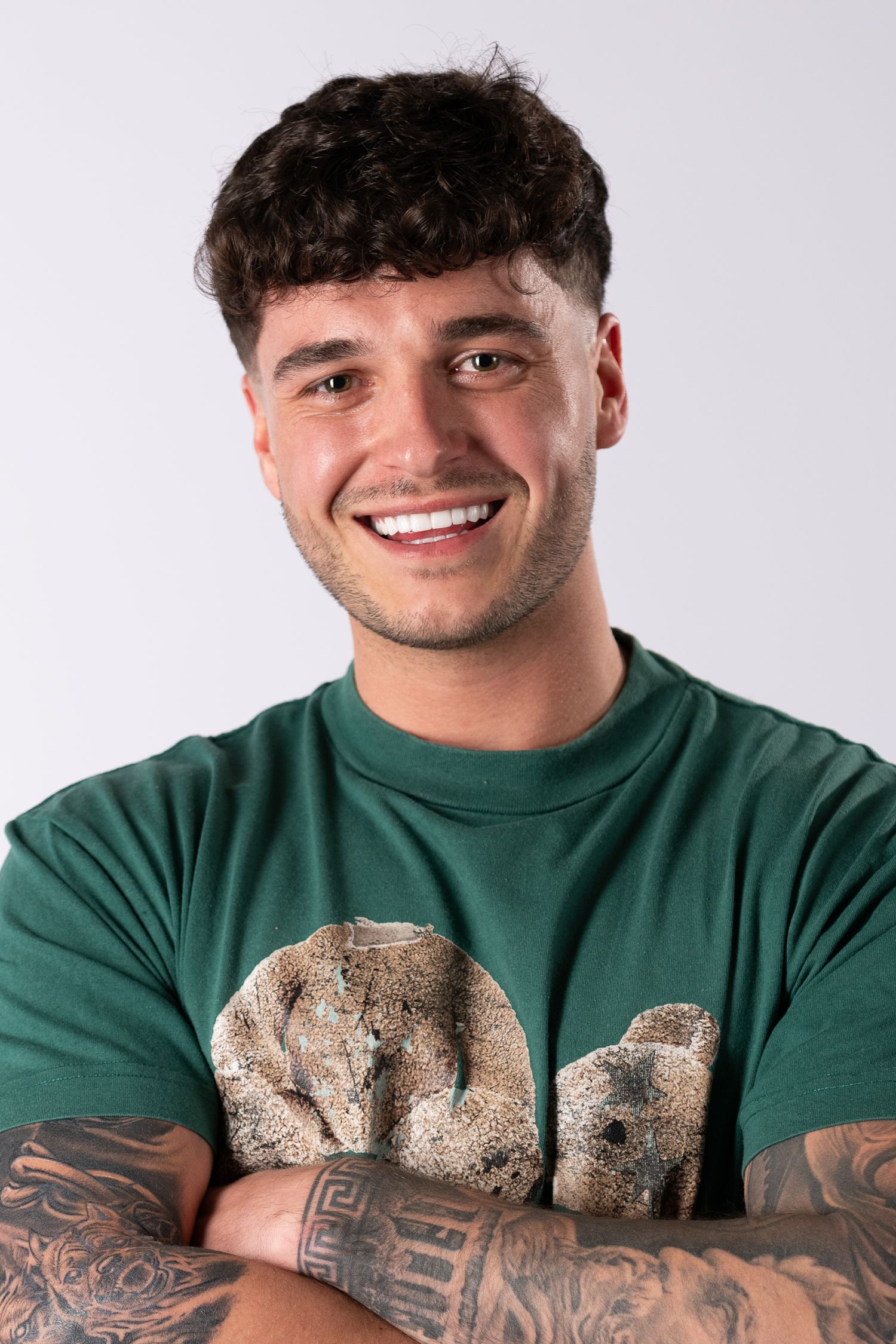 Person in green sweater showing off detailed arm tattoos while smiling at the camera.