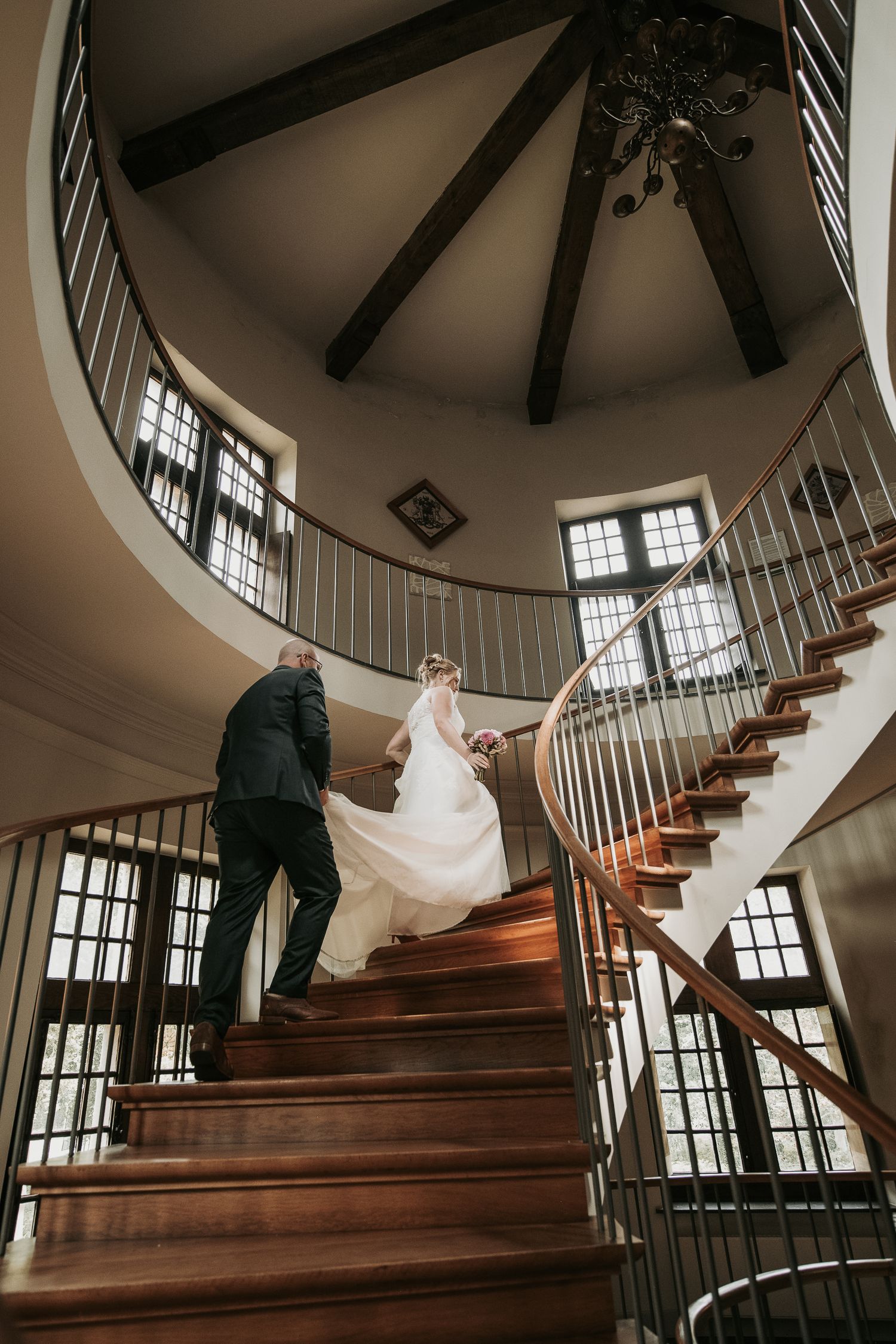 A sequence of photos showing a couple ascending a curved wooden staircase in a historic building with large windows.
