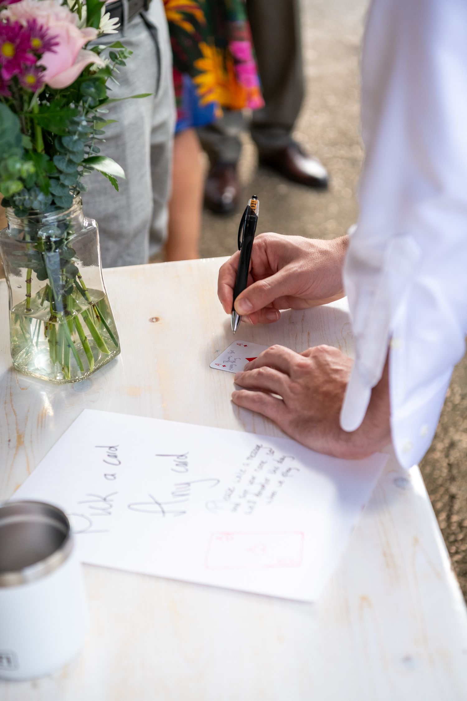 Someone signs a document at a table with fresh flowers in a vase and a coffee cup nearby.