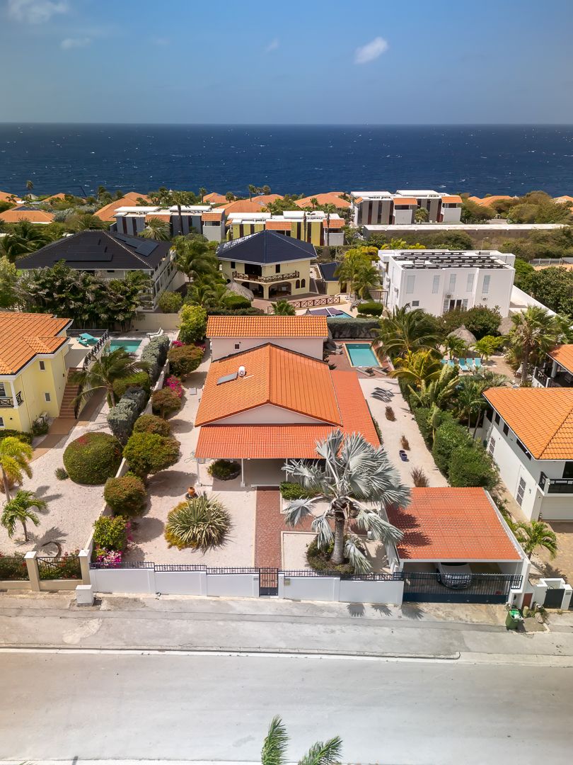 Aerial view of a Caribbean villa with orange tile roofs, pool, and lush gardens near the turquoise ocean.