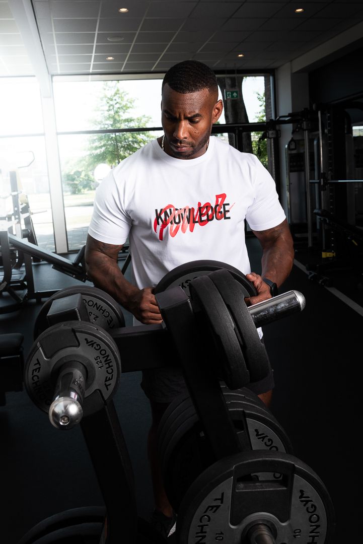 Athletic person in a white t-shirt with red lettering lifting dumbbells at a well-equipped indoor gym.