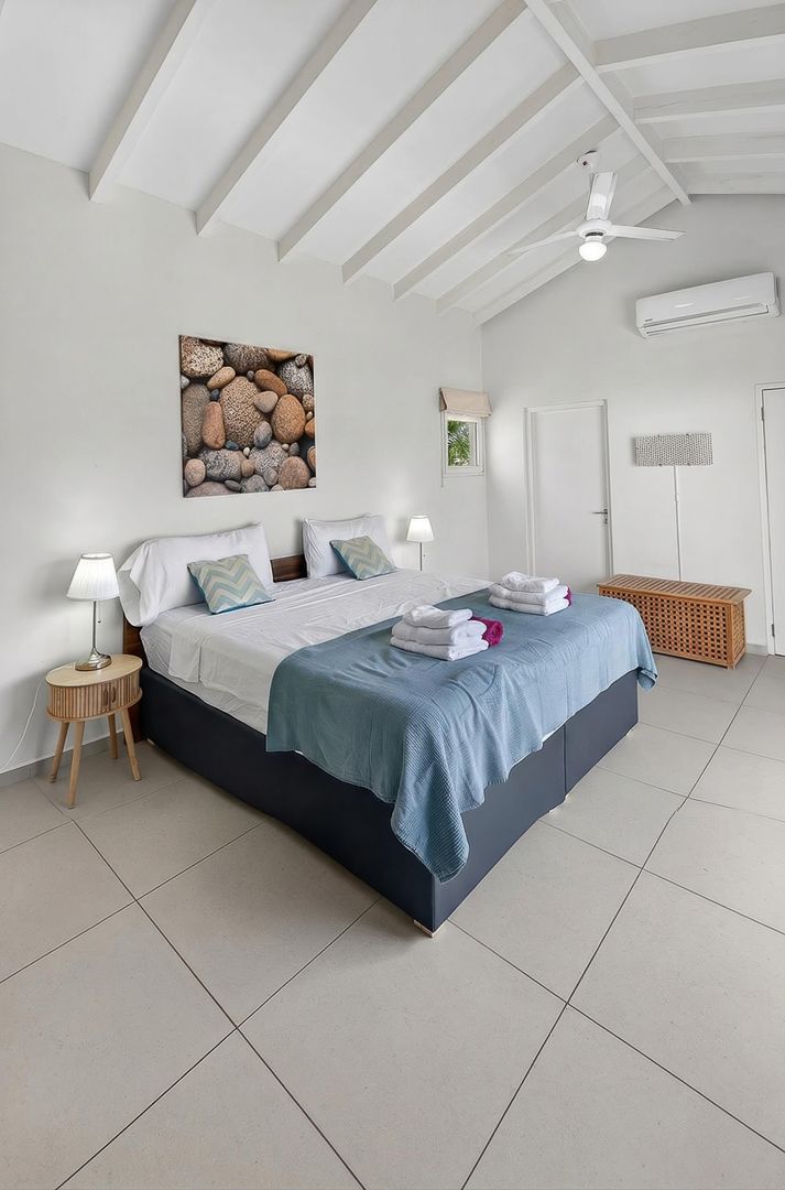 Spacious bedroom with vaulted white ceiling, ceiling fan, teal bedding, stone artwork, and large tiled floors.