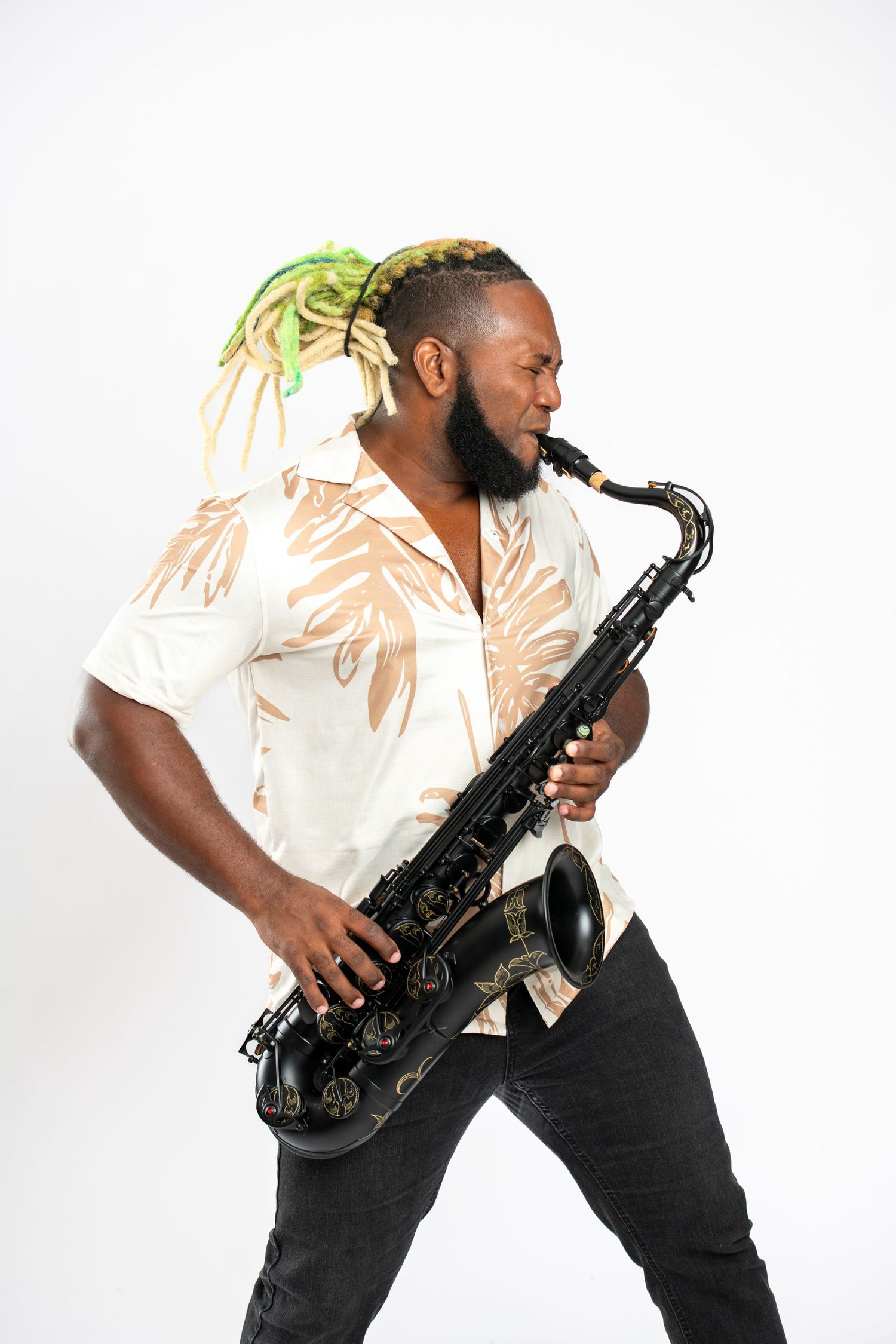 Man with green dreadlocks playing black saxophone, wearing floral shirt, against white background.