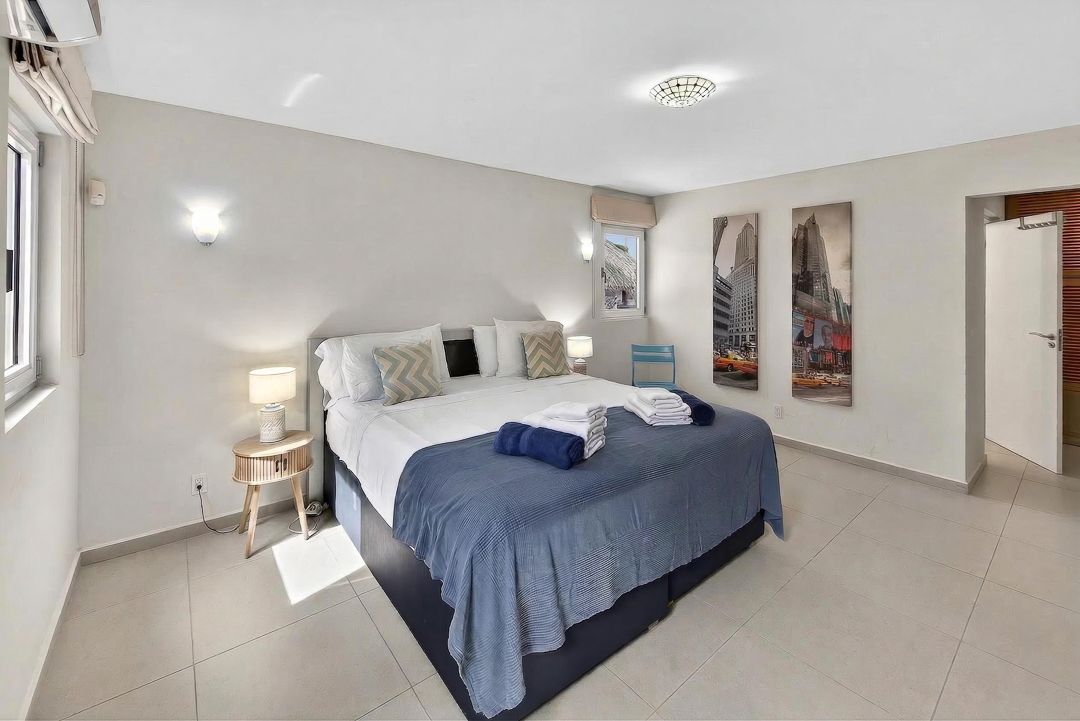 Bright modern bedroom with blue bedding, tiled floors, bedside lamps, and a New York canvas print on the wall.