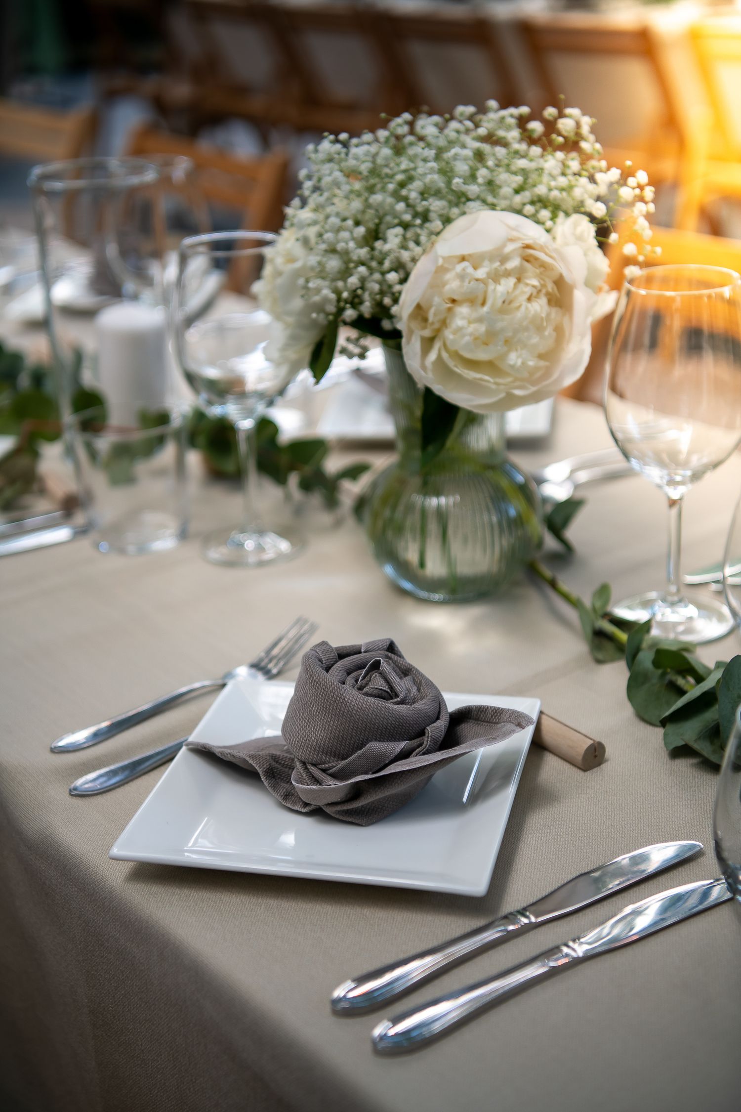 Elegant table settings with white baby's breath flowers, gray napkins, and silver cutlery on light tablecloths.