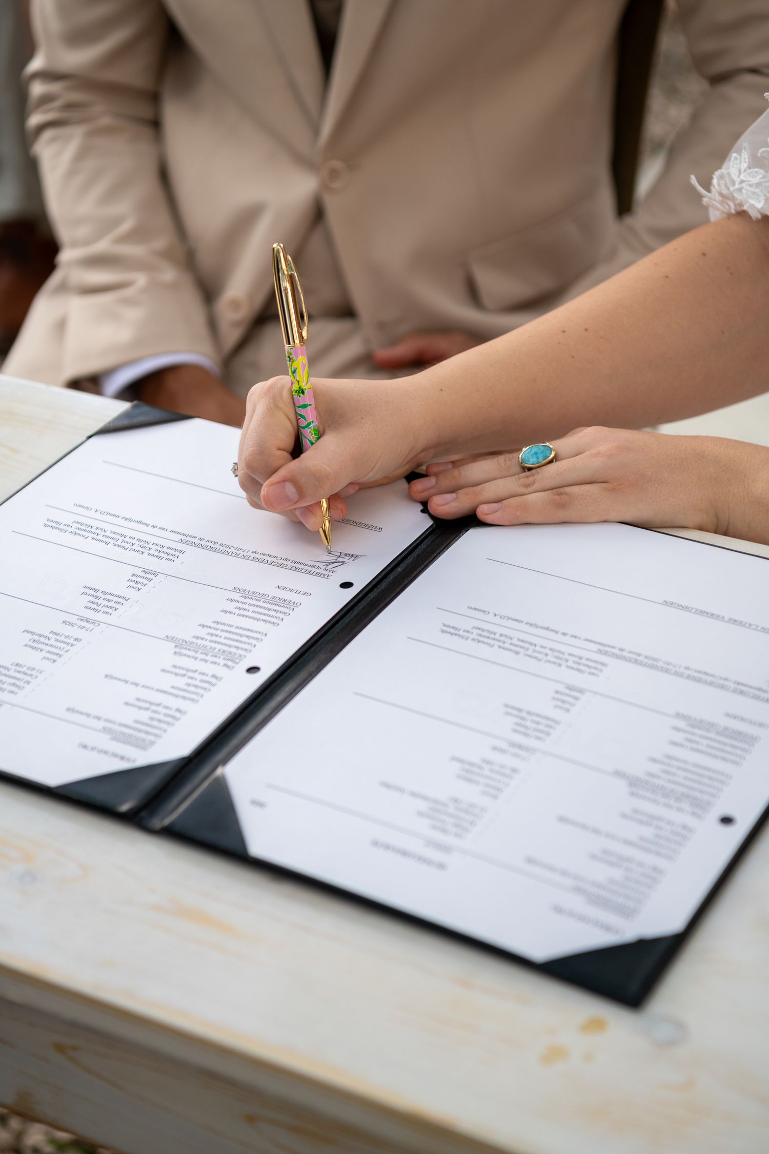Close-up view of hands signing documents with pens on a white desk surface.