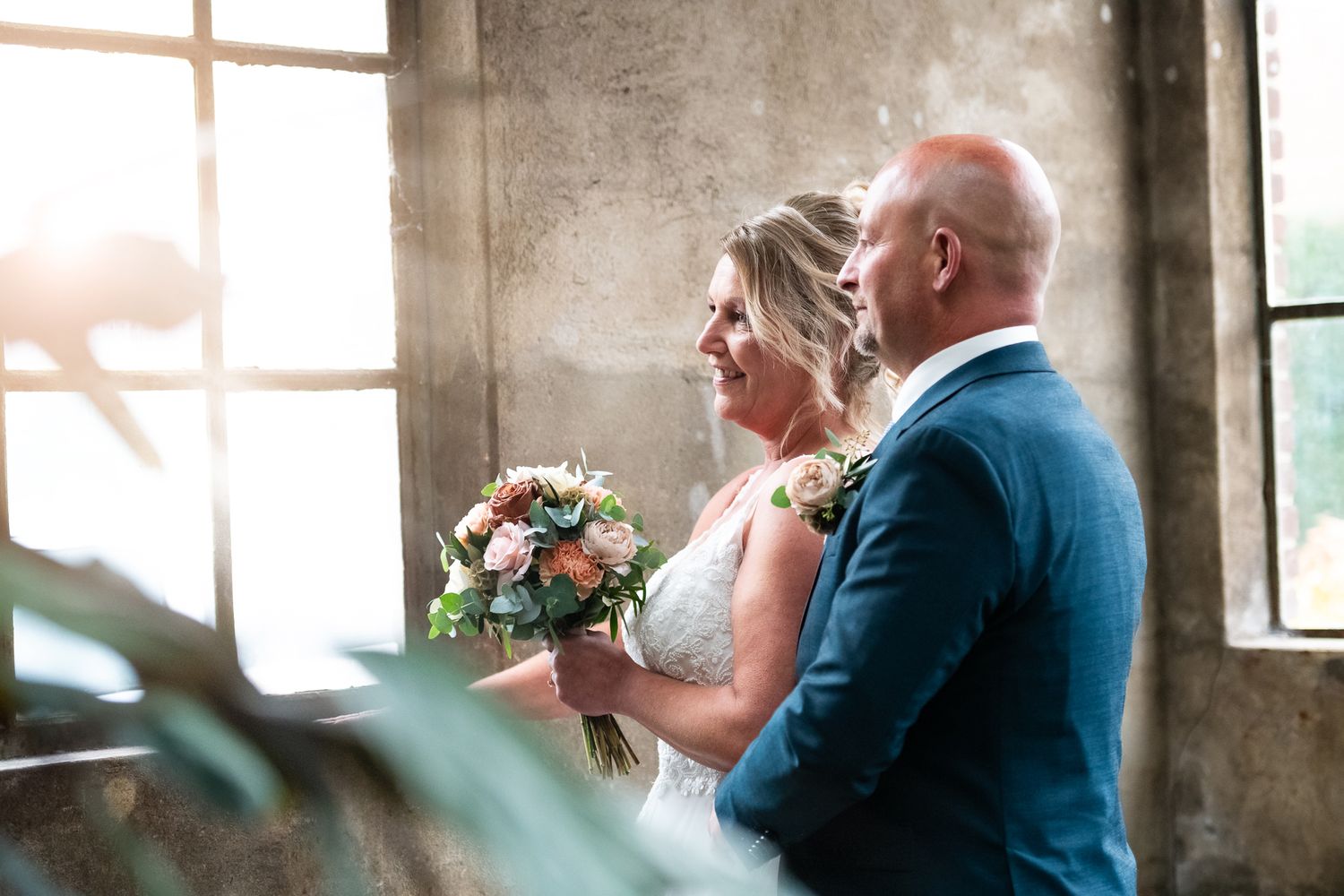 A couple shares an intimate moment during their wedding ceremony in a rustic venue with natural light streaming through windows.