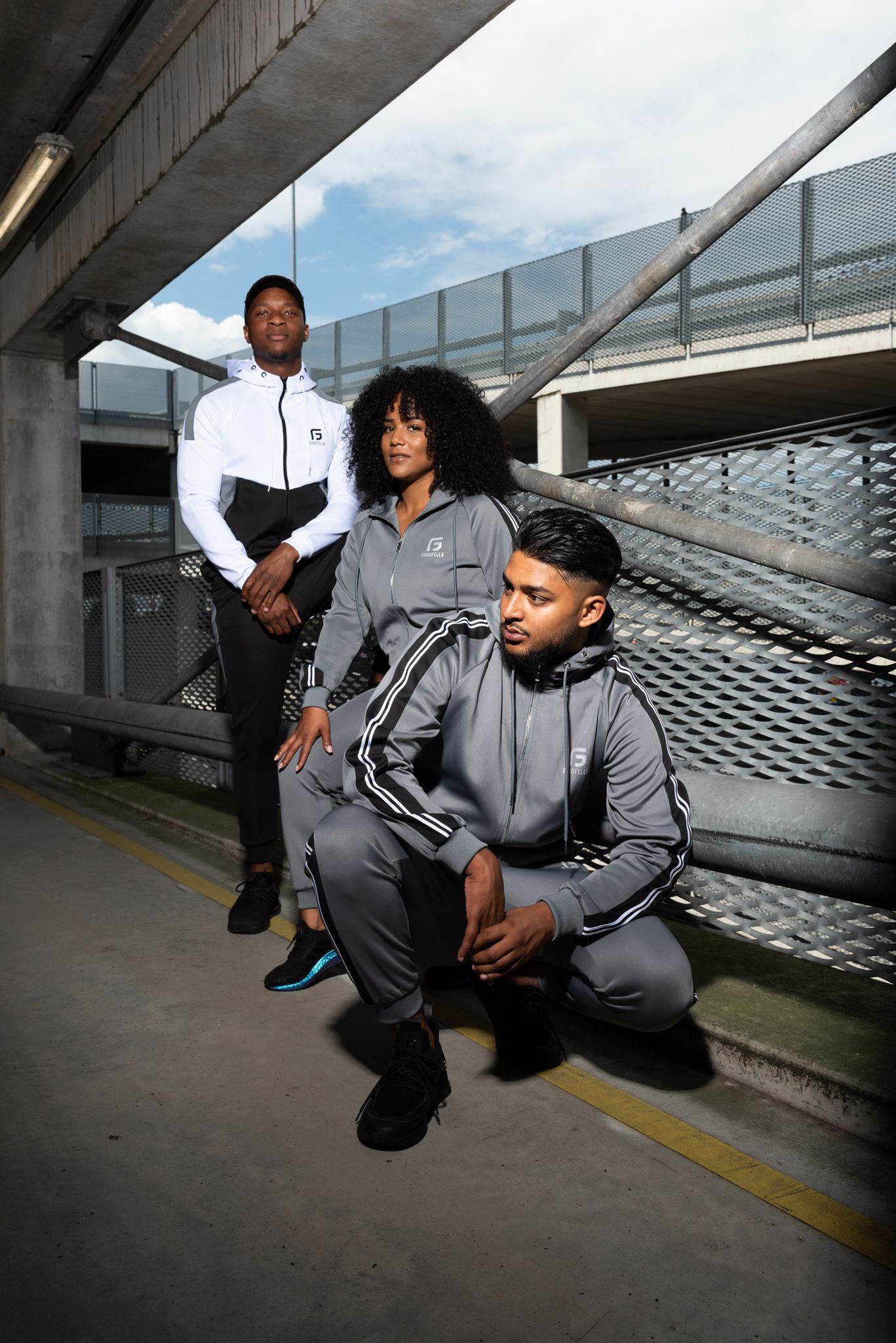 Athletic figures in grey tracksuits perform dynamic dance movements in a concrete urban setting.