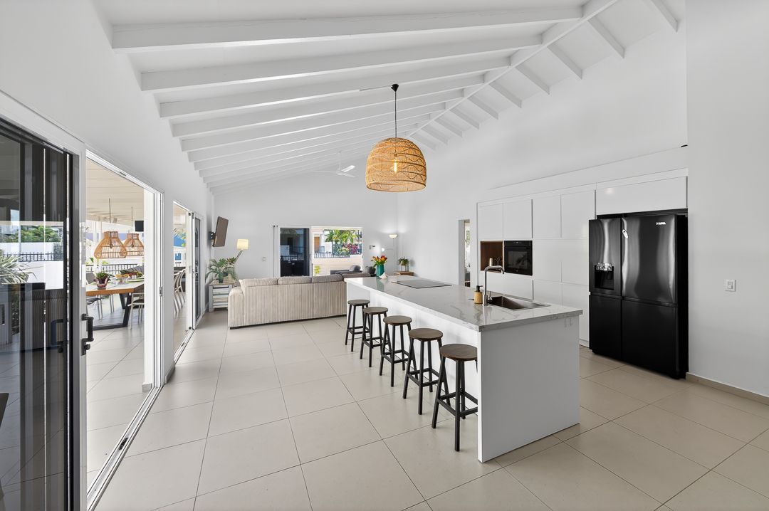 Modern white kitchen with vaulted beam ceiling, island bar with stools, pendant light, and black French door refrigerator.