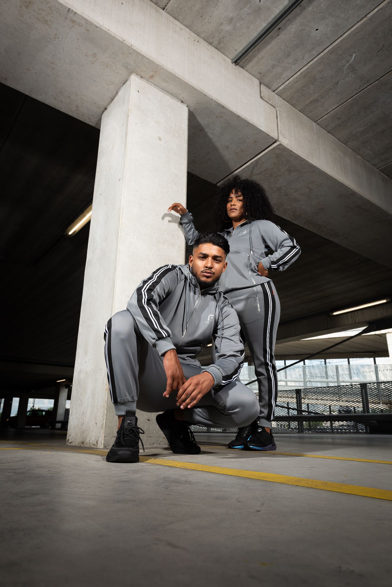 A person in gray athletic wear crouches low in a concrete parking garage, creating a dynamic urban composition.