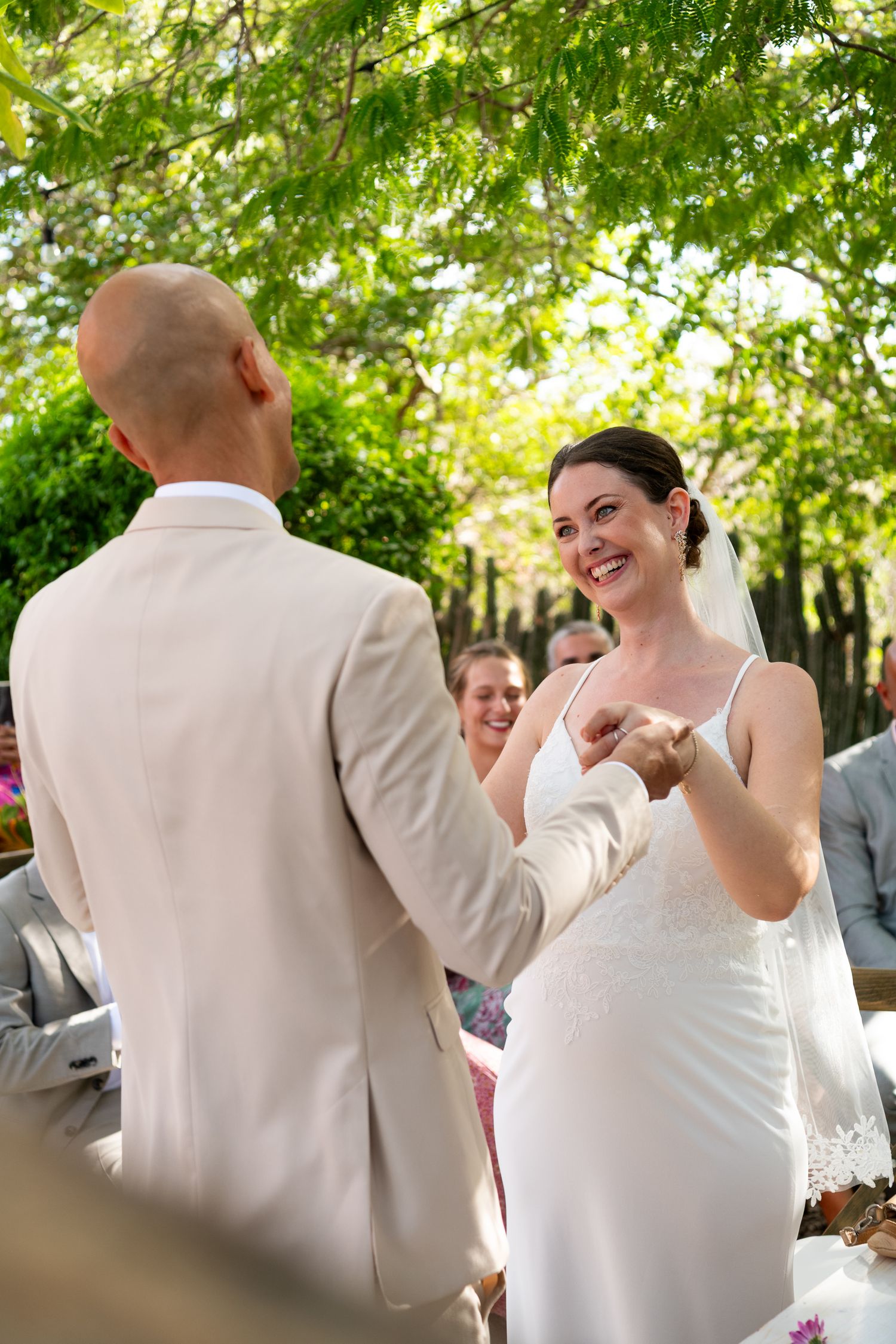 A couple shares a joyful dance moment at an outdoor wedding reception under green leafy trees.