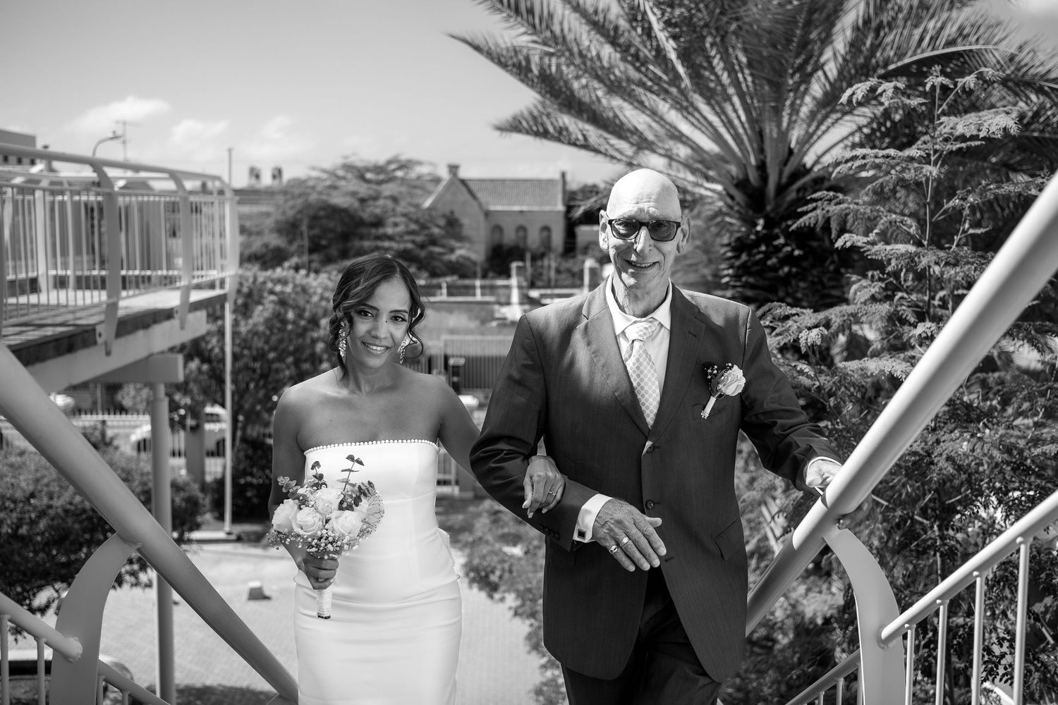 Wedding party members pose together on a tropical balcony with palm trees in the background.