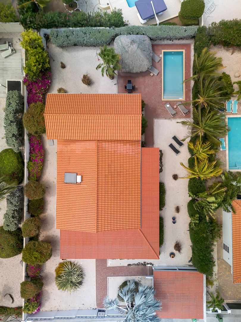 Aerial view of a Mediterranean villa with orange terracotta roof, swimming pool, and lush tropical landscaping.