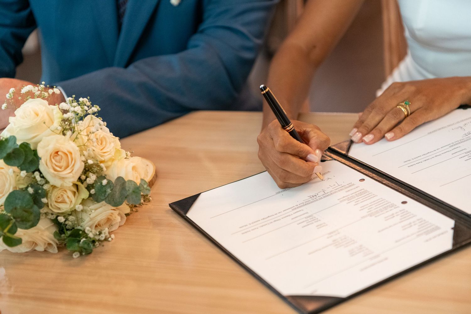 Signing of wedding documents with a peach rose bouquet on wooden table during marriage ceremony.