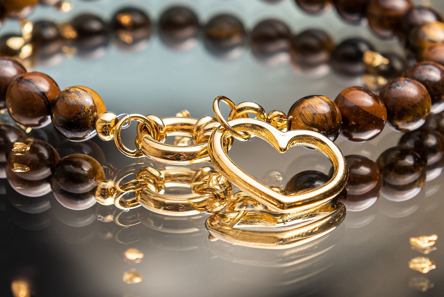 Close-up macro shot of brown wooden prayer beads with gold metal clasp on dark reflective surface.
