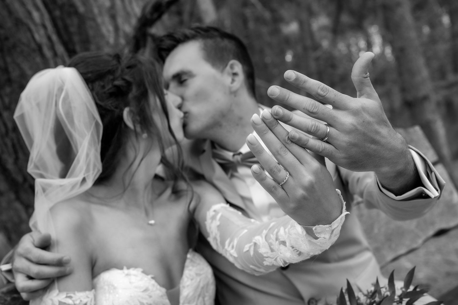 A tender black and white wedding moment captured as newlyweds share a kiss and embrace outdoors.