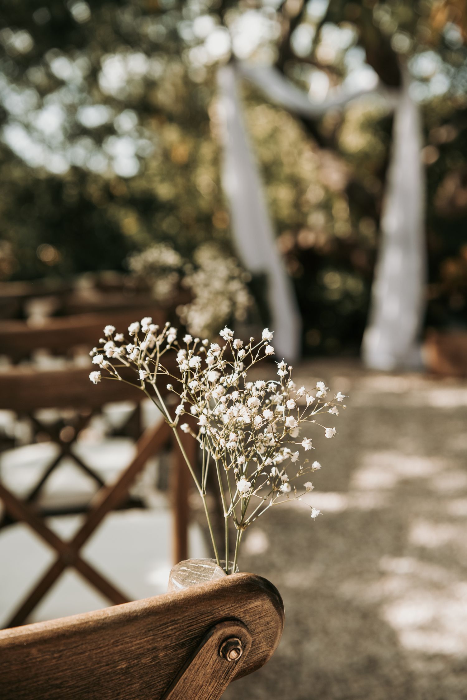 Delicate white baby's breath flowers arranged in small glass vases on wooden surfaces at an outdoor event setting.