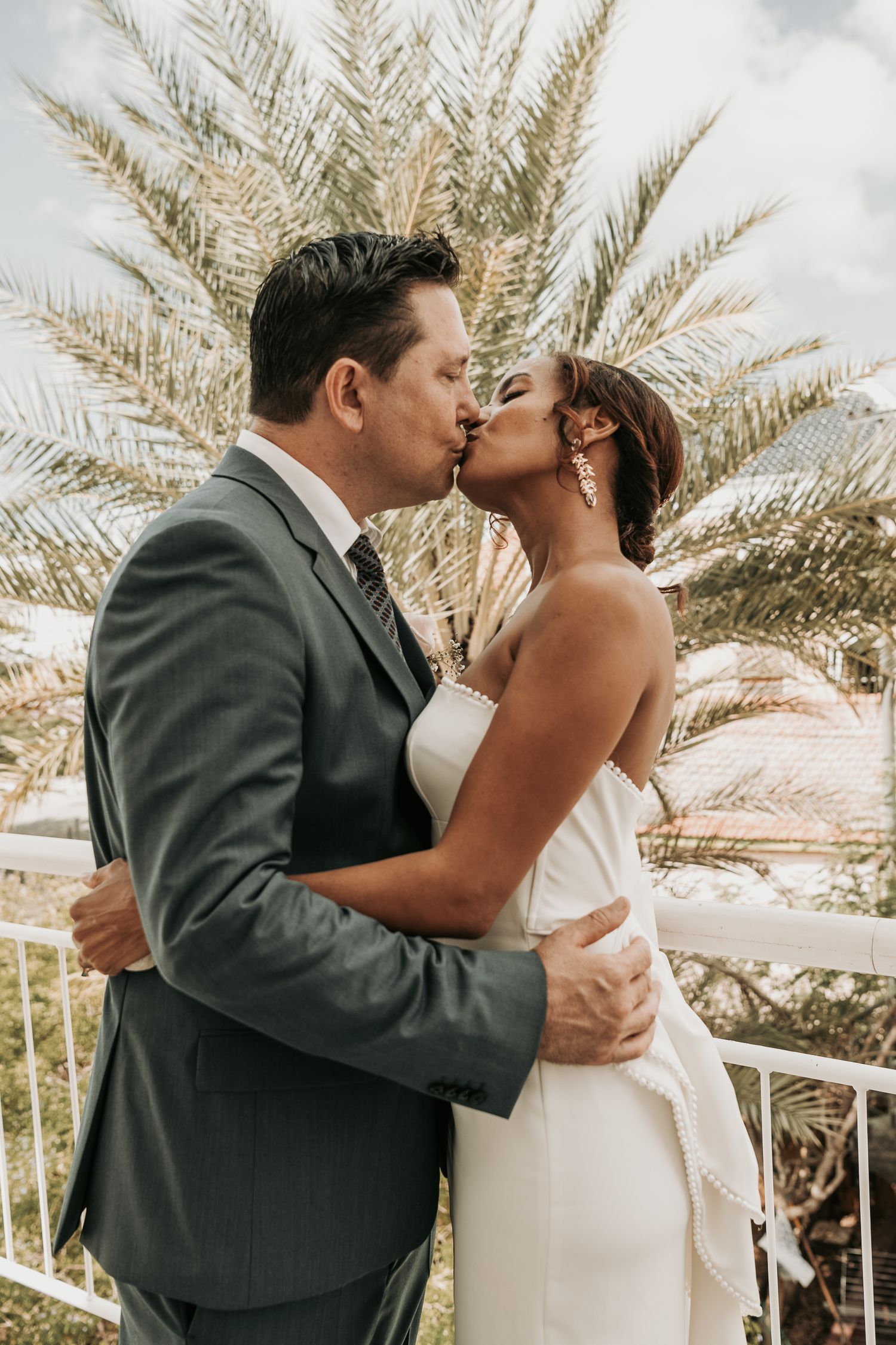A romantic wedding kiss sequence with palm trees in the background at a tropical destination venue.