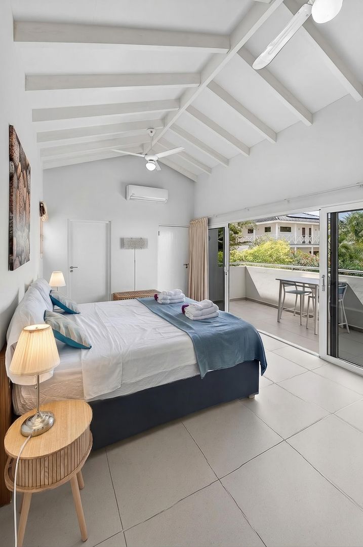 Bright hotel bedroom with vaulted white ceiling, king bed with blue accents, ceiling fan, AC unit, and balcony access.