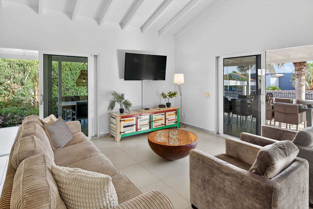 Bright living room with beamed ceiling, wall-mounted TV, colorful sideboard, wood coffee table, and sliding doors to outdoor patio.