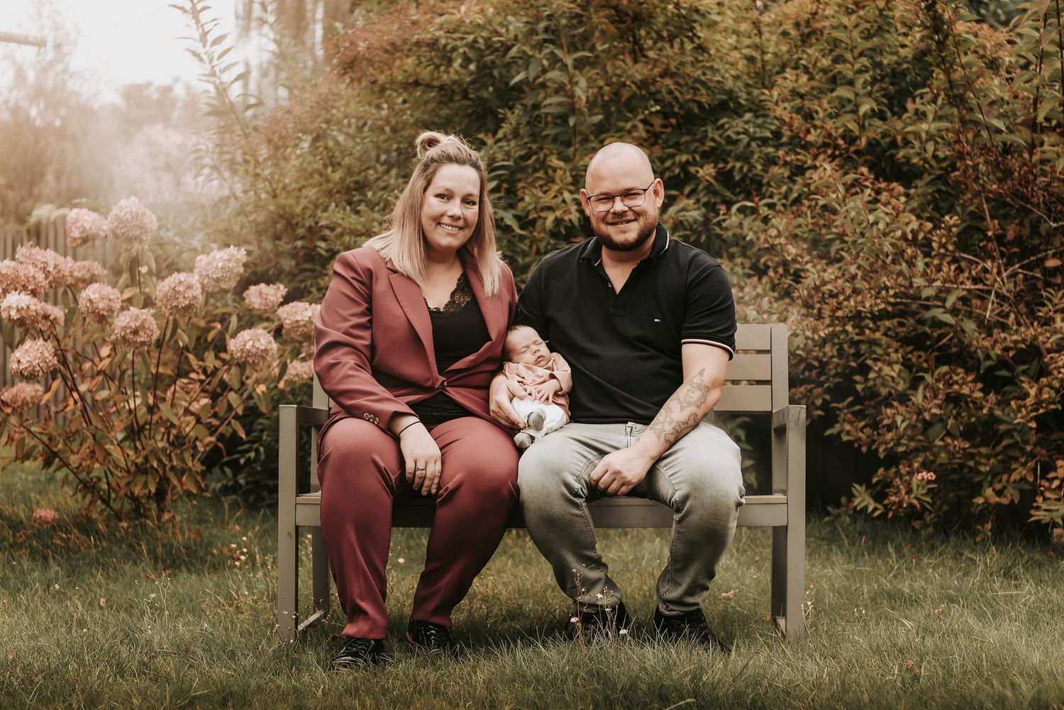 A couple sits together on a wooden garden bench surrounded by autumn foliage and soft sunlight.