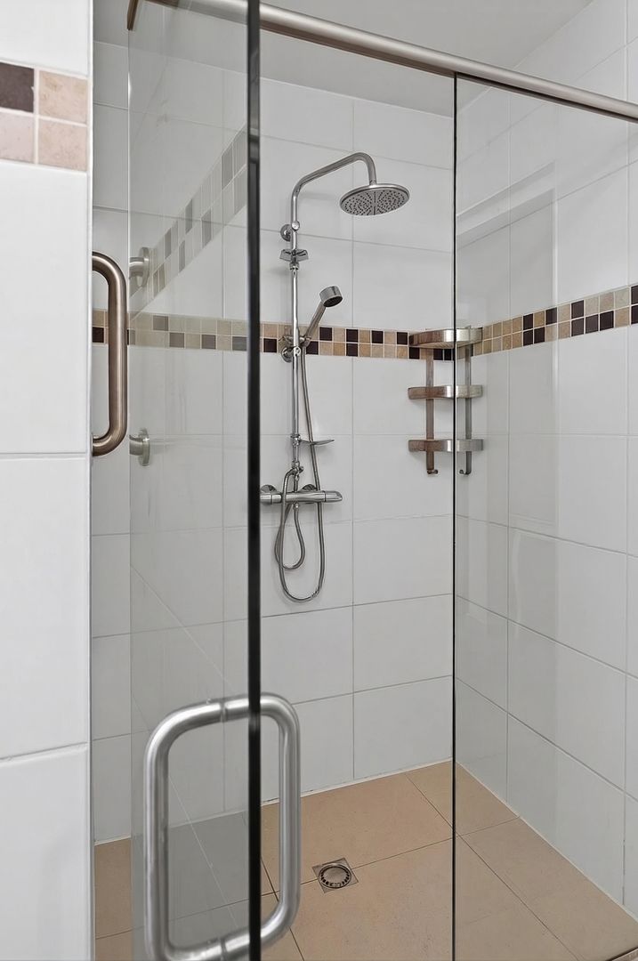 Modern walk-in shower with rain head, handheld fixture, glass door, mosaic tile border, and white wall tiles.